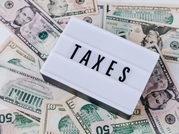 A sign saying taxes lays on top of American dollars. 